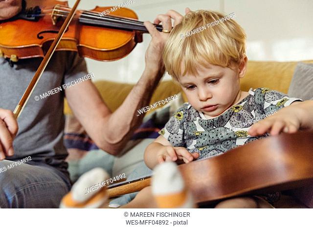 Portrait of toddler testing ukulele while his father playing violin