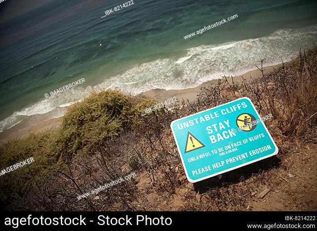 Stay back warning sign on cliff edge near ocean