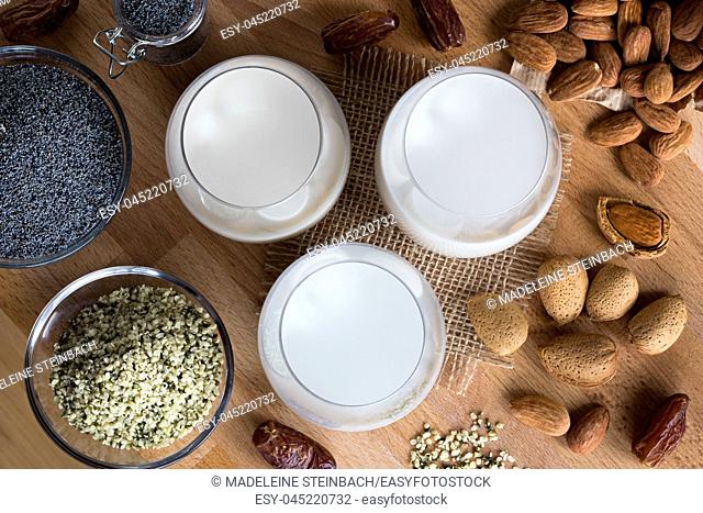 Top view of three glasses of vegan plant milk - almond milk, poppy seed milk and hemp seed milk, with shelled and unshelled almonds, poppy seeds
