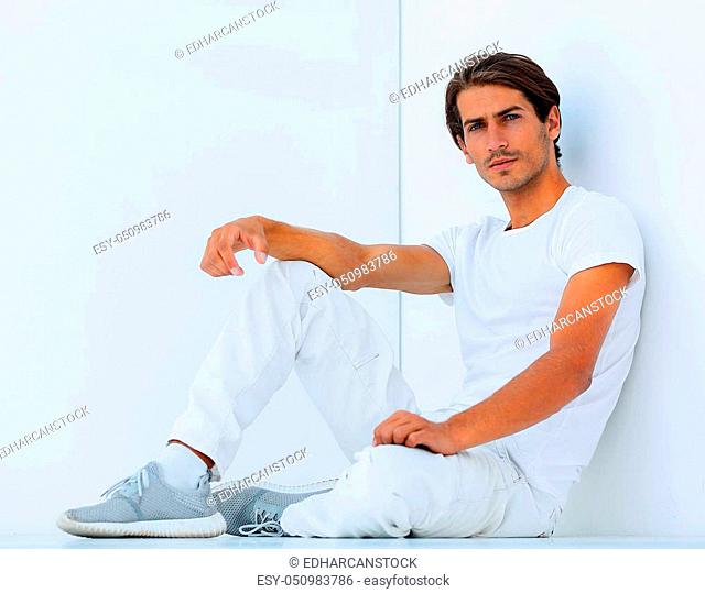 sad young man sitting beside a white wall. photo with copy space