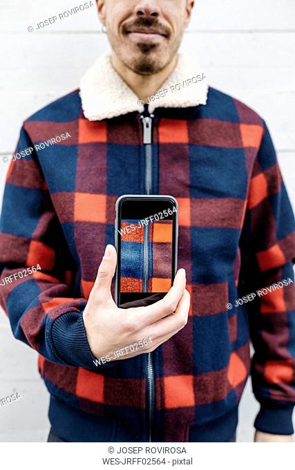Young man showing a photo on the phone in the colors of his jacket