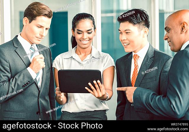 Pan Asian and Caucasian business team looking at tablet computer watching presentation of new project in front of modern corporate office