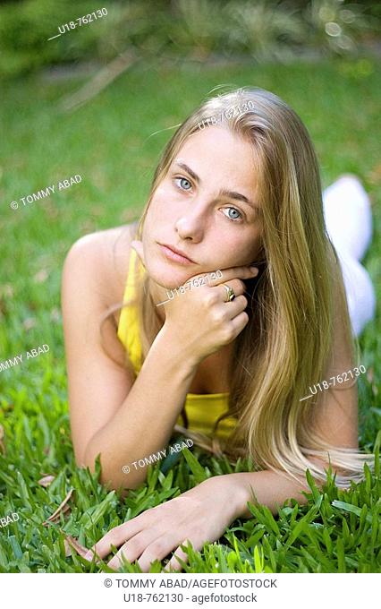a young blonde girl laying down in the grass with a yellow shirt