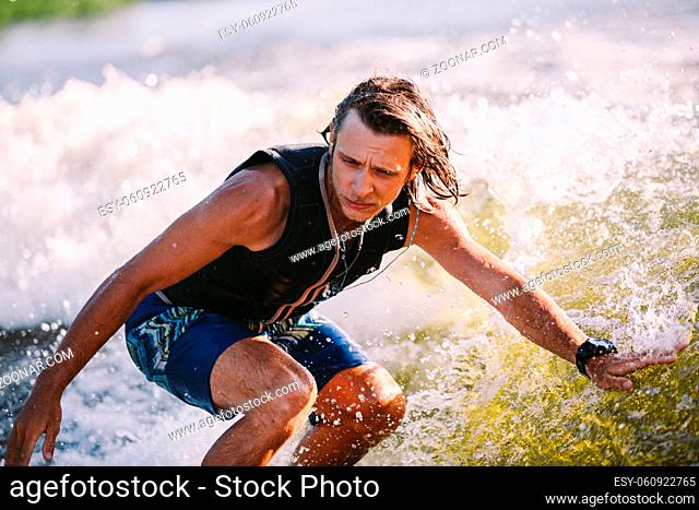 Active wakesurfer jumping on wake board down the river waves. Surfer on wave. Male athlete training on wakesurf training