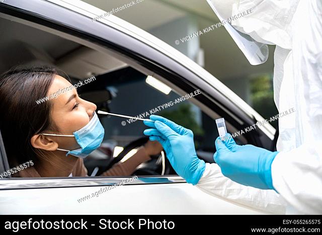 Portrait of asian woman drive thru coronavirus covid-19 test by medical staff with PPE suit by nose swab. New normal healthcare drive thru service and medical...