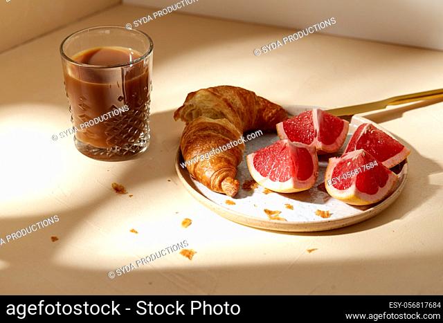 glass of coffee, croissant and grapefruit on table
