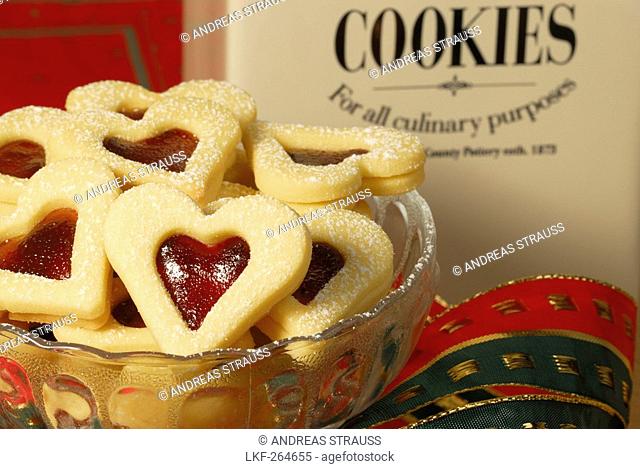 Christmas cookies raspberry hearts covered with sugar piling up in glasbowl, Christmas decoration in background