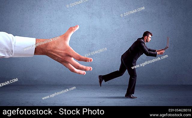 Young miniature businessman running from a big hand with blueish grey background