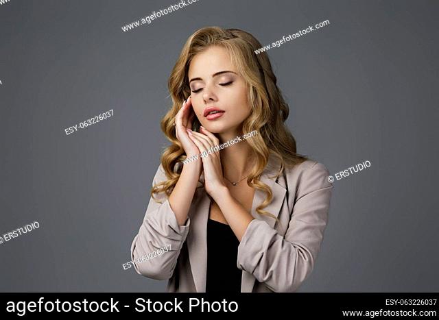 Portrait of young beautiful woman in showing sleep gesture on gray background