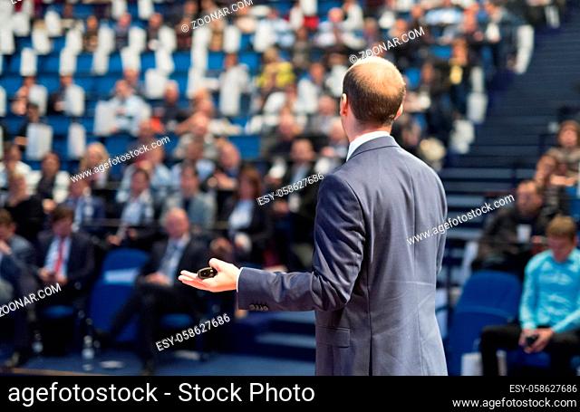 Rear view of speaker giving a talk on corporate business conference. Unrecognizable people in audience at conference hall