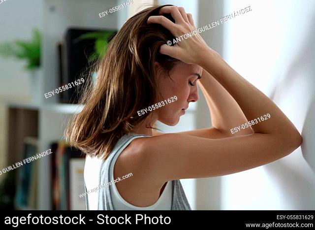 Side view portrait of a sad woman complaining leaning on a wall at home in the night