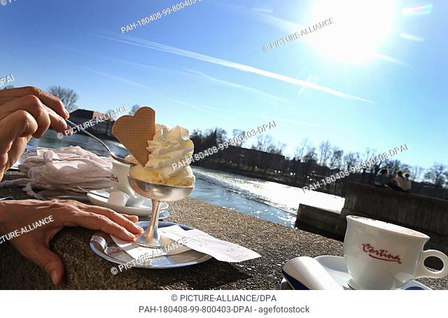 07 April 2018, Germany, Landsberg am Lech: A vanilla ice cream with cream and two cups of coffee on a wall outside an ice cream parlour