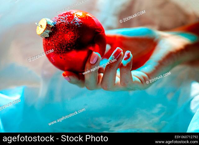 woman holding new year ball ornament decoration. christmas ice ball in hand close up on cold blue background