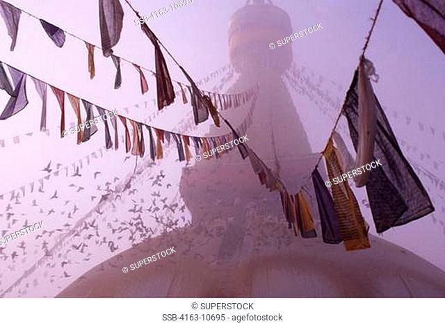 NEPAL, KATHMANDU, BOUDHNATH, TIBETAN STUPA TEMPLE IN FOG, PRAYER FLAGS, PIGEONS
