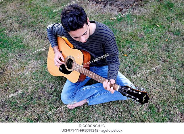 Young man playing a guitar in a garden. France