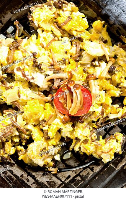Scrambled eggs with enoki mushrooms and onions in pan, close up