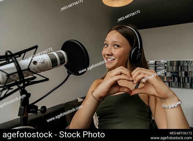 Smiling teenage girl making heart shape while singing in recording studio