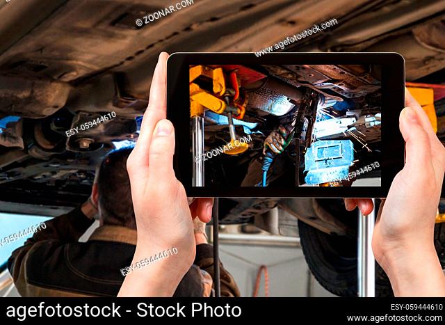 travel concept - visitor photographs of welding the silencer on car by argon welding during repairing in workshop on smartphone