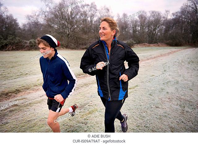 Mother and son running on frosty grassland looking away smiling