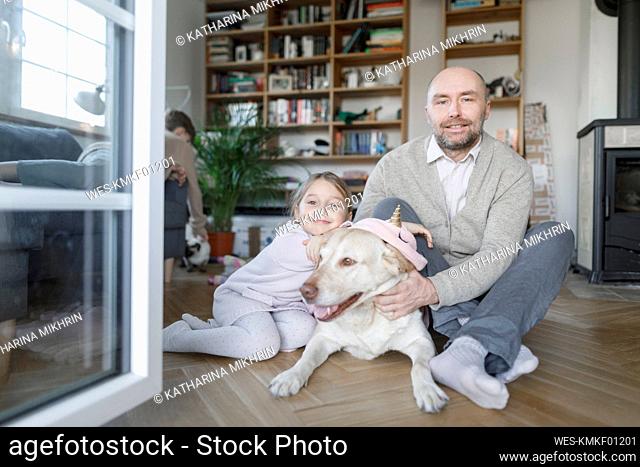 Portrait of father sitting with his little daughter and the dog on the floor at home