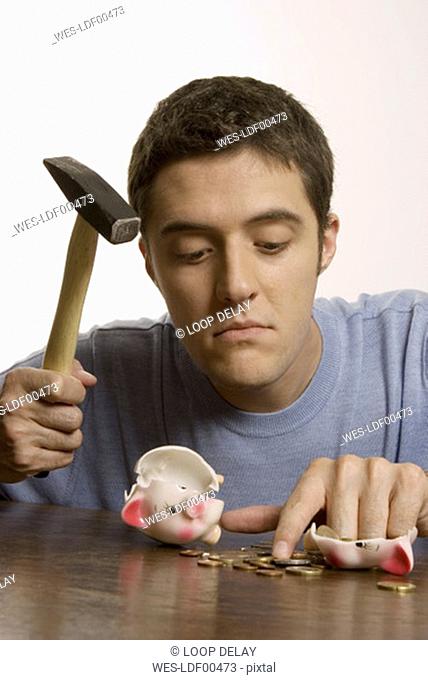 Young man with hammer and broken piggy bank