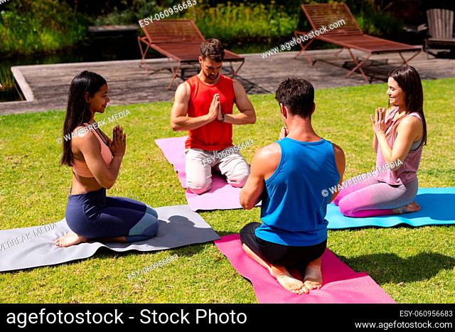 Men and women meditating on exercise mats in public park on sunny day