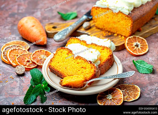 Slices of spicy cake with cottage cheese cream and a spoon in a ceramic plate on a textured brown background, selective focus
