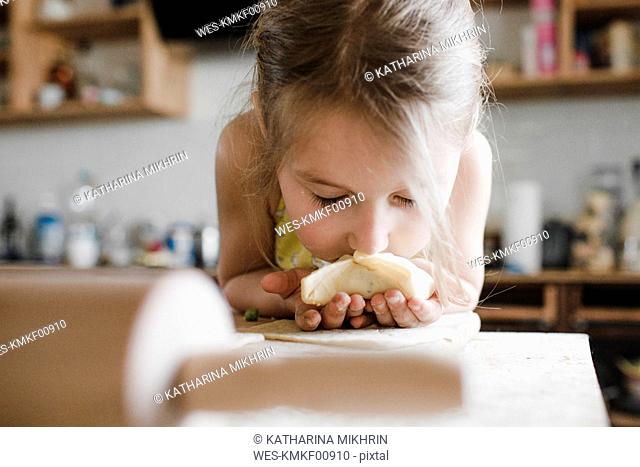 Little girl smelling freshly prepared stuffed pastry