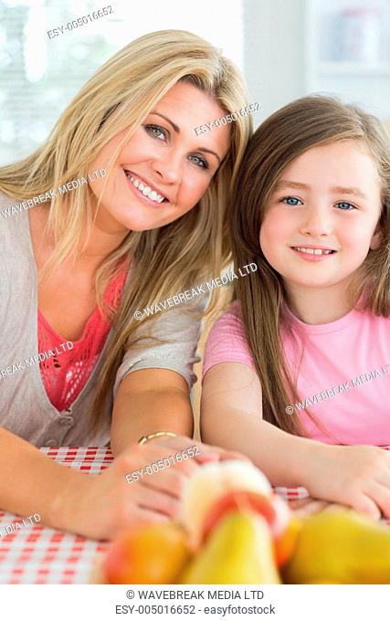 Mother and child sitting at kitchen table smiling with fruit bowl on table