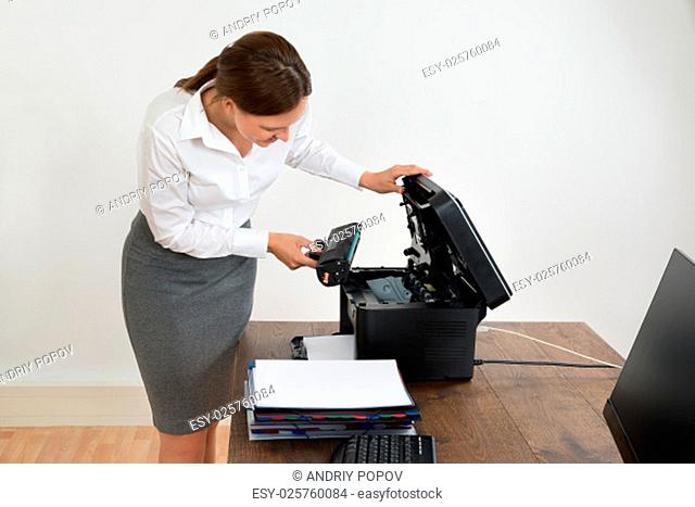 Young Businesswoman At Desk Putting Laser Toner Cartridge In Printer