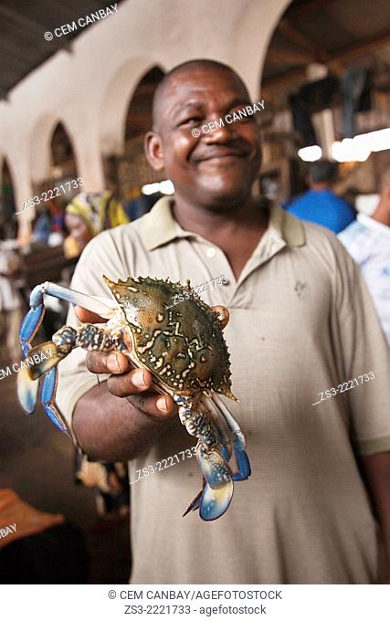 Vendor holding a crab with blue legs in his hand at the daily market on Darajani road, Stone Town, Unguja Island, Zanzibar Archipelago, Tanzania, East Africa