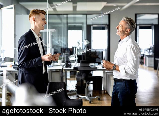 Smiling businessmen discussing while standing at open plan office