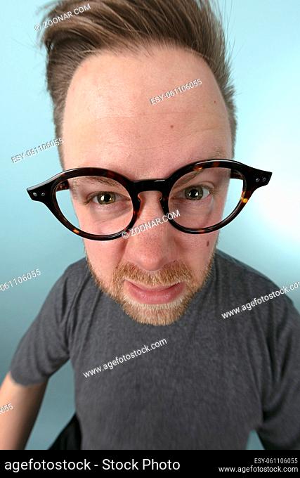 Man wearing large glasses stretching forwards to peer into the lens in a distorted perspective emphasising his eyes and glasses in a fun portrait