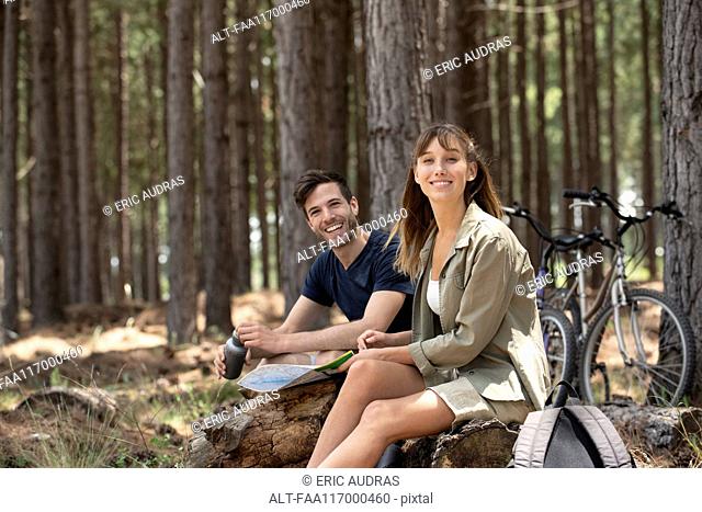 Smiling young couple sitting on log in pine forest