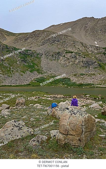 Woman resting on rock by lake while hiking in Herman Gulch, Colorado