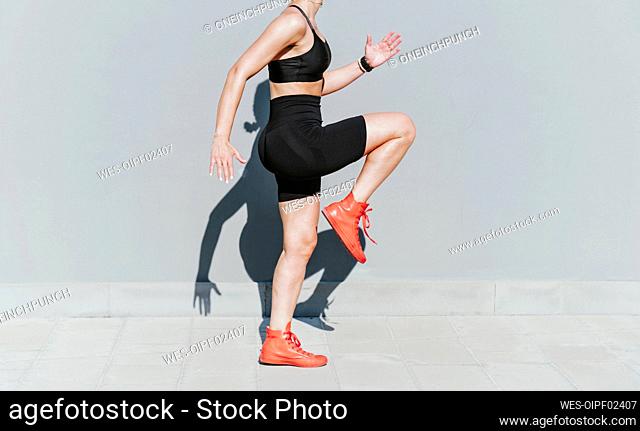 Woman exercising by gray wall on sunny day