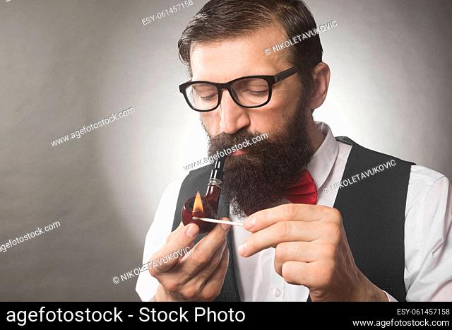 The bearded hipster is igniting his tobacco pipe, smoking pipe concept