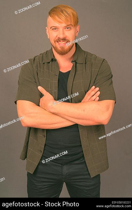 Studio shot of bearded man with blond hair wearing casual clothes against gray background