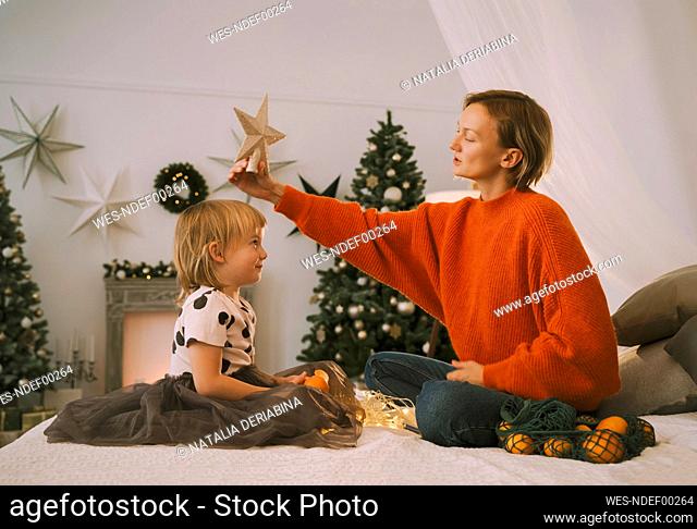 Mother putting star on daughter's head in bedroom