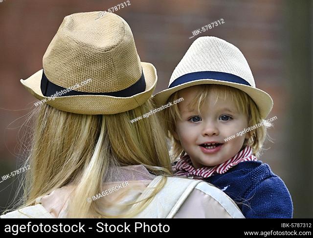 Mother holding son, 19 months, in her arms, both wearing similar hat, Stuttgart Baden-Württemberg, Germany, Europe