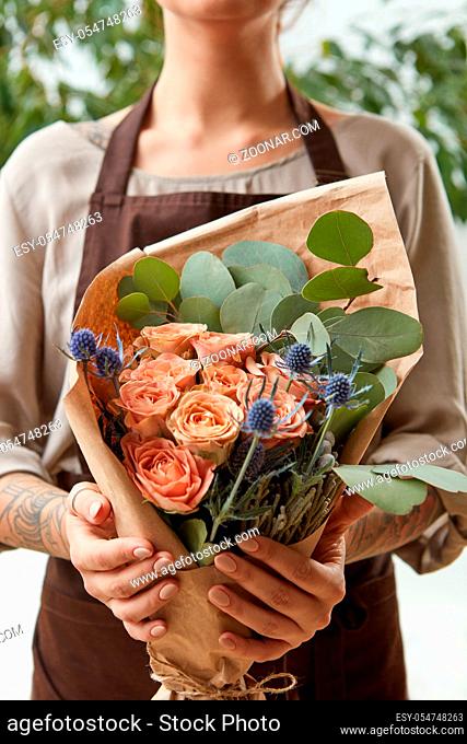 Florist woman with a bouquet of coral roses and green leaf. Girl is holding a flowers in her hands. The gift to Mother's Day