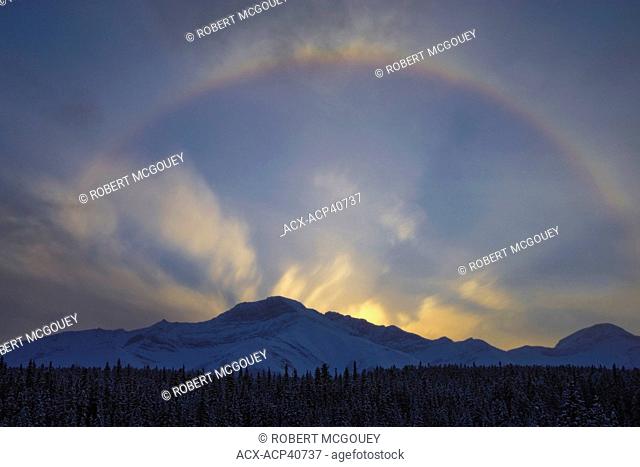 Mountain backlit by the reflecting sky, colorful circle and backlit clouds after the sun goes down in the Rocky Mountains of Alberta Canada