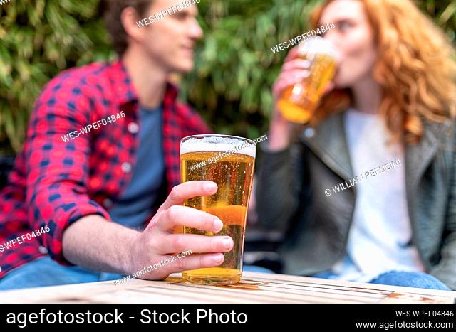 Man holding beer glass while sitting with girlfriend at pub