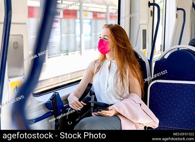 Businesswoman in protective face mask looking through window while commuting in train