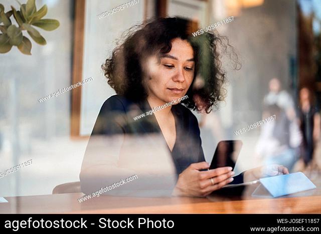Woman using smart phone seen through glass at cafe