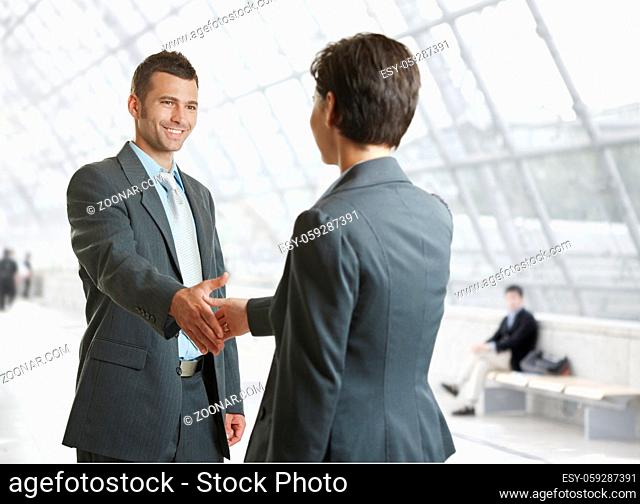 Smiling businessman and businesswoman shaking hands in hallway