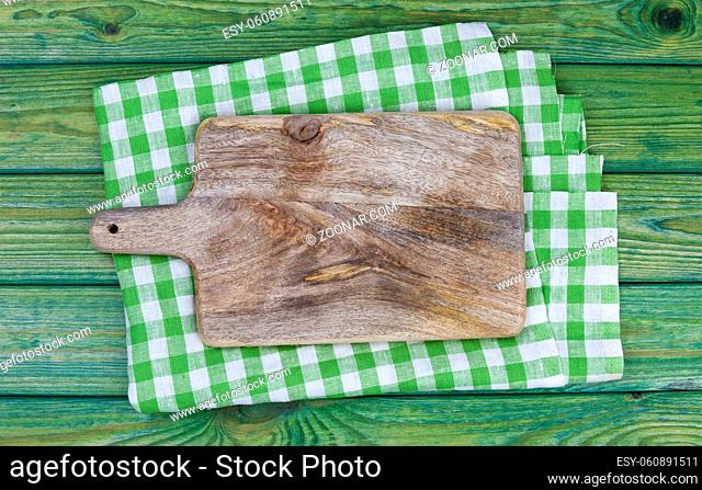 Old cutting board on wooden table with green checkered tablecloth, top view with copy space
