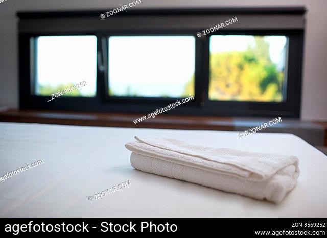 Close-up shot of a fresh white towel on the bed in hotel room, window with nature scene in background