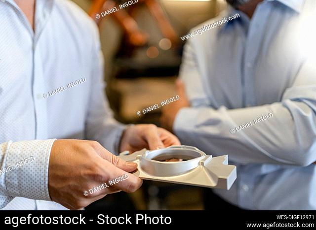 Businessman examining object while standing with colleague at factory