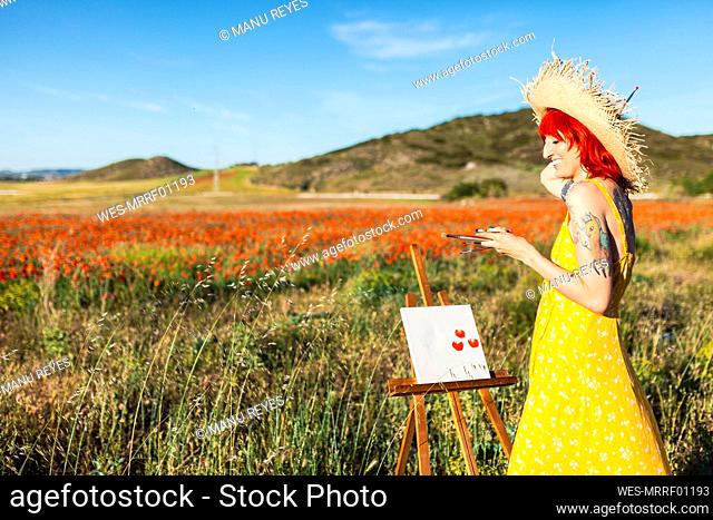 Smiling woman standing by canvas at field on sunny day